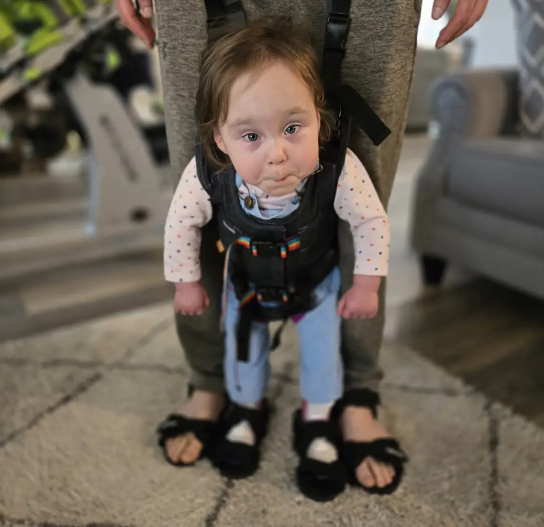 Charli supported upright in a gait trainer or harness.